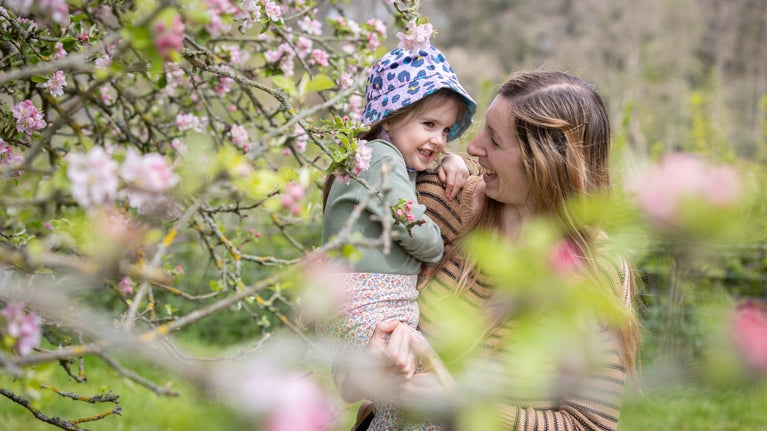 A woman carrying a child amongst the pink blossom branches.